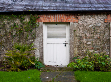 A wooden door of a stone house on the grounds of the Blarney Castle.