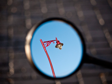 A red lamppost is reflected in a rearview mirror.