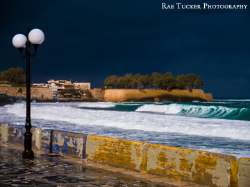 Turquoise-colored waves crash under dark storm clouds in Chania, Greece.