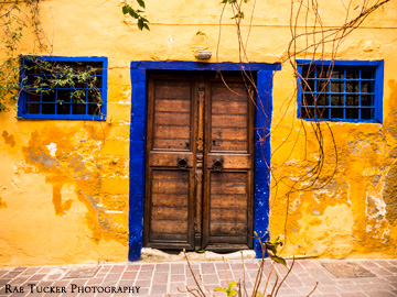Bold yellows and blues on a wall with double, wooden doors and windows.