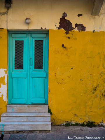 An old wall, painted yellow, offsets a teal-colored entrance.