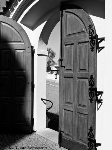 A black and white image of wooden doors that lead to a church courtyard.
