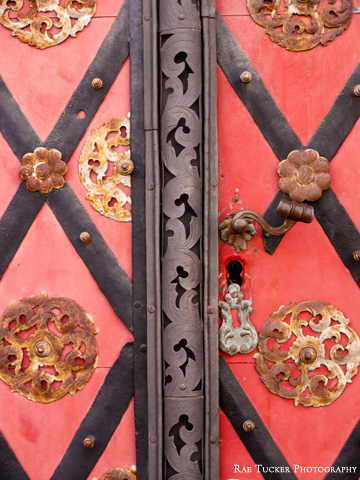 An ornate, red, metal door shows signs of wear and rust.
