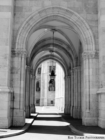 A black and white image of light and shadows filtering through an arched walkway outside of the Hungarian Parliament building in Budapest.