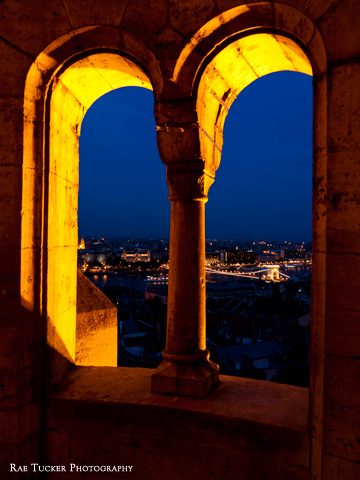Windows at Fisherman's Bastion look over Budapest and the Chain Bridge in the early evening.