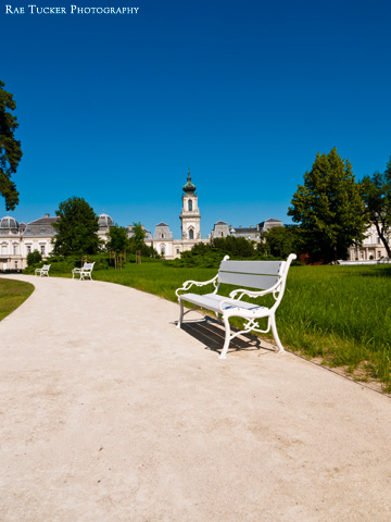 A white park bench on a path leading to the Festetics Palace in Keszthely, Hungary