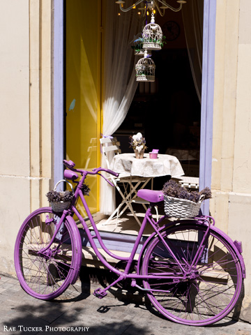 A purple-painted bicycle carries a white basket full of lavender.