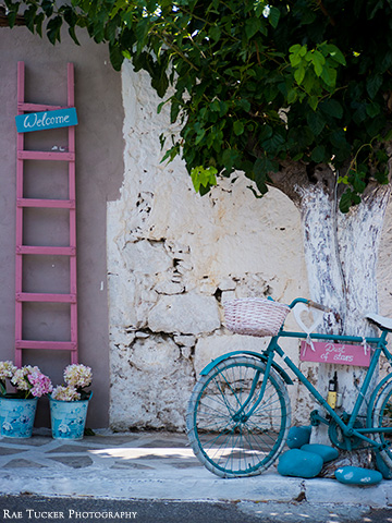 A pink latter with a welcome sign, potted flowers and a blue and white bicycle