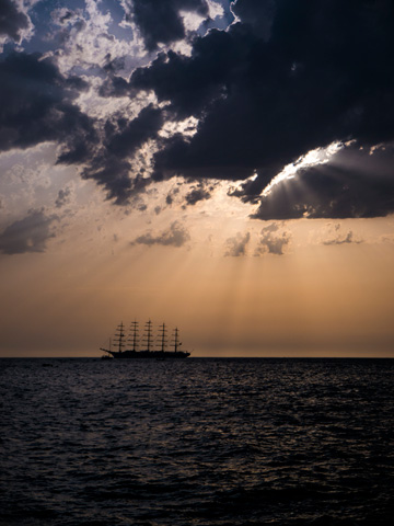 Light from the setting sun shines through storm clouds over a tall ship on the Adriatic Sea