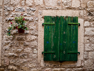 Green, wooden shutters and a small plant adorn a stone wall in Kotor, Montenegro