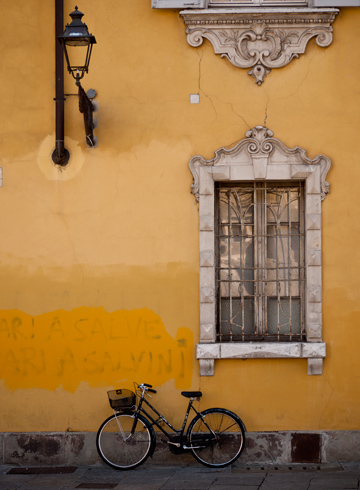 Ornate window, lantern and bicycle on a yellow wall in Parma, Italy