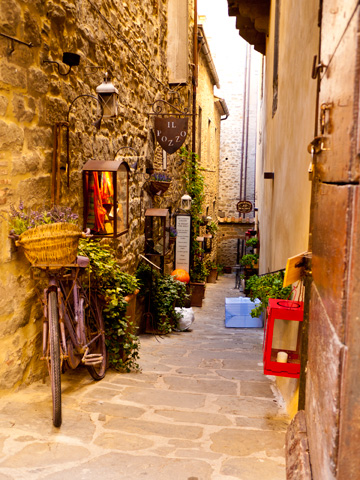 Plants, a bicycle, lanterns and other objects litter a street in Cortona, Italy
