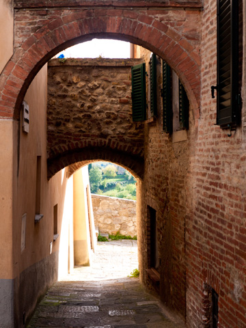 A street covered with stone and brick arches leads to the city walls of Montepulciano, Italy