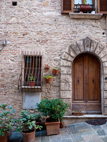 A medieval, stone building with a wooden door and potted plants in Montepulciano, Italy.