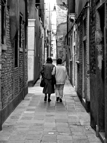 Two friends walk with linked arms in this black and white image taken in Venice, Italy