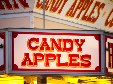 A neon sign over a candy apple kiosk at a carnival