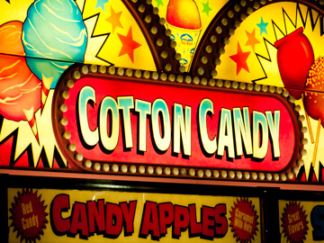 Cotton candy and candy apples advertised on a neon sign at a carnival