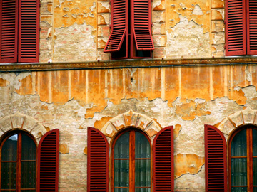 Red shutters adorn these arched windows on an apartment building in Siena, Italy