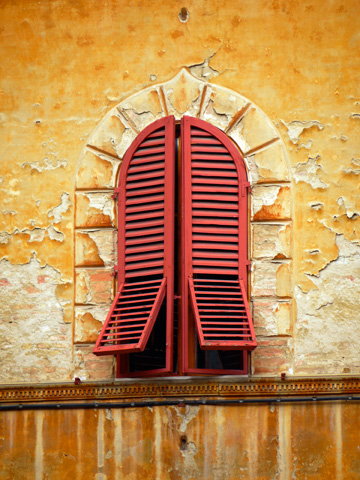 A building in Siena, Italy with a red shuttered window and peeling paint