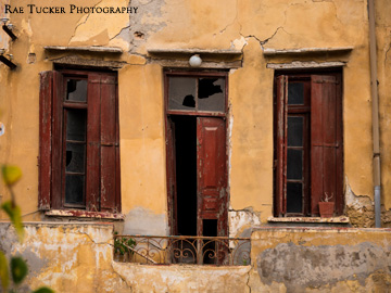 An abandoned balcony with broken wooden shutters and windows.