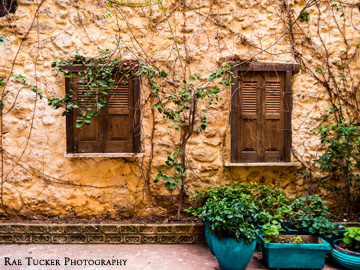 A stone wall, wooden shutters over windows and teal-colored potted plants.