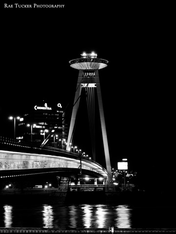 The New Bridge in Bratislava spans the Danube river in this black and white photograph taken at night.