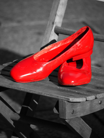 A bright red pair of shoes on a wooden chair.